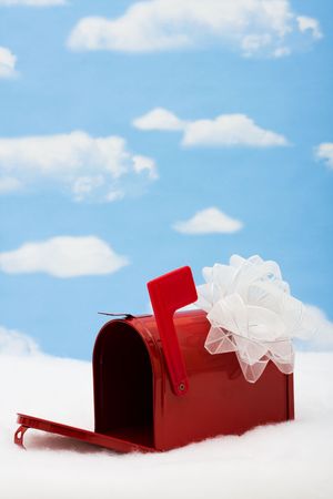 Red mailbox with white ribbon bow and the flag up sitting on snow with a sky background, mailboxの写真素材