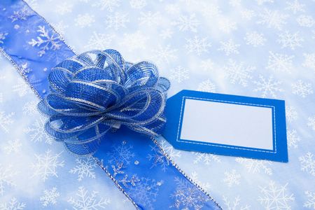 Blue ribbon and blank gift tag on snowflake background with bow making a presentの写真素材