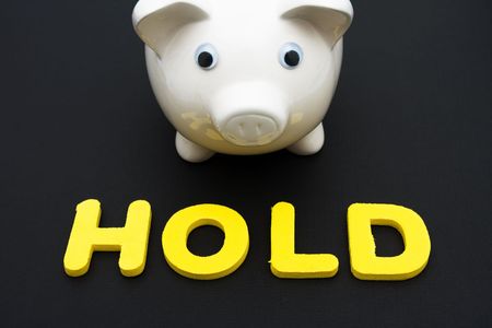 Piggy bank with letters spelling hold on black background, investing your savingsの写真素材