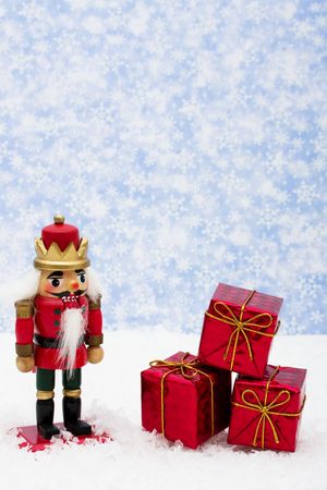 Nutcracker sitting on snow with three red presents on a snowflake background, nutcrackerの写真素材