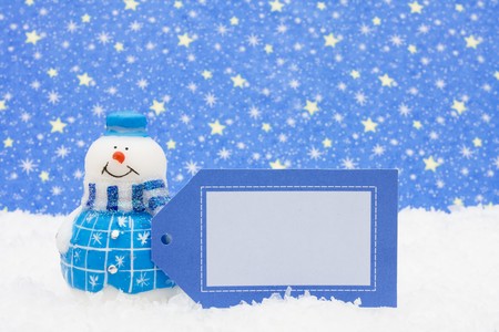 Snowman sitting on snow holding blank gift tag with a star background, Snowmanの写真素材