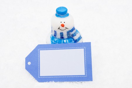 Snowman sitting on snow holding blank gift tag with a star background, Snowmanの写真素材