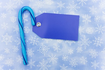 Blue candy cane with a blank gift tag sitting on a blue snowflake background, candy caneの写真素材