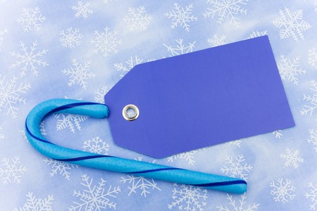 Blue candy cane with a blank gift tag sitting on a blue snowflake background, candy caneの写真素材