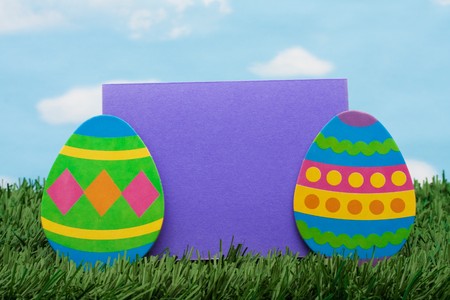 Easter eggs and a purple blank card on green grass background, Easter basket