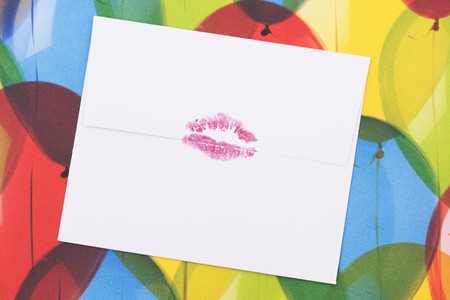 A white envelope with a red lipstick kiss sealing it sitting on a colourful balloon background, sealed with a kissの写真素材