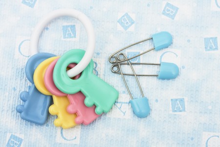 Blue diaper pins and rattle sitting on a blue alphabet background, diaper pin and rattleの写真素材