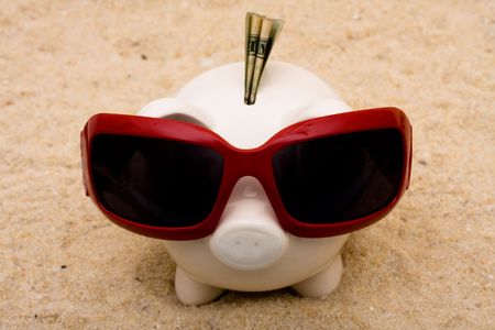 A piggy bank wearing sunglasses on a sand background, vacation savingsの写真素材