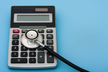 A calculator and stethoscope isolated on a blue background, calculating healthcare costsの写真素材