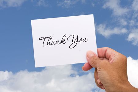 A thank you card sitting in hands on a sky background, blank cardの写真素材