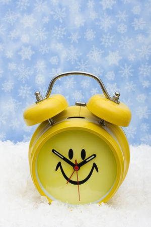 A yellow smiley face clock sitting on snow background, winter timeの写真素材