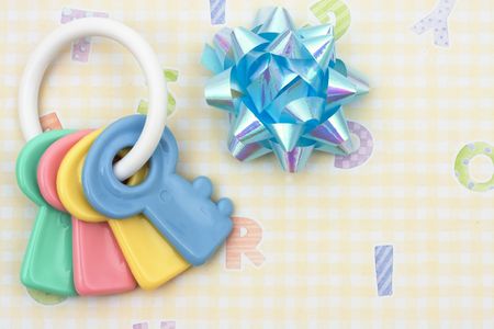 Key shaped baby rattle with blue bow sitting on a yellow alphabet background, baby rattle