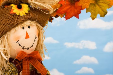 A scarecrow sitting on fall leaves on a sky background, scarecrowの写真素材