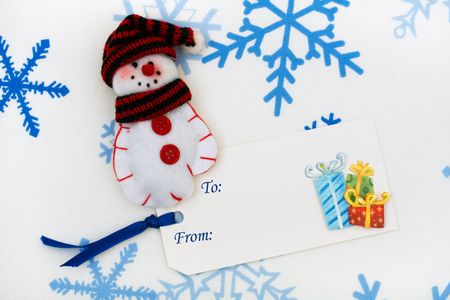 A snowman mitten sitting together with a blank gift tag on a snowflake background, happy holidaysの写真素材