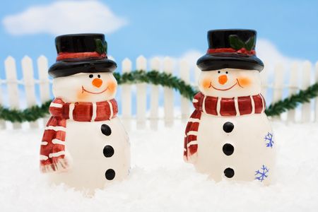 A snowman on a white picket fence with garland on a  sky background, winter sceneの写真素材