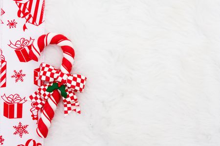 A candy cane with a red present ribbon on a white fur backgroundの写真素材