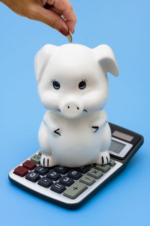 A piggy bank sitting on a calculator on a blue background, Adding to your Savingsの写真素材
