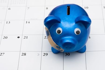 A blue piggy bank with adhesive bandage on a calendar, Are you hurting paying your billsの写真素材