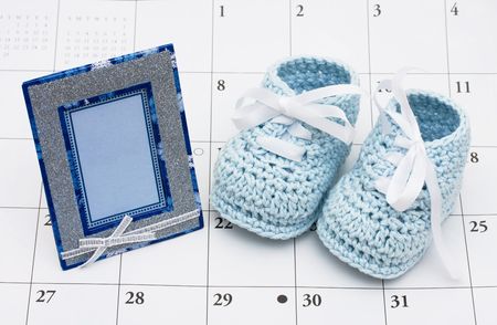 An empty picture frame with a pair of baby booties on a white calendar background, Welcoming a new babyの写真素材