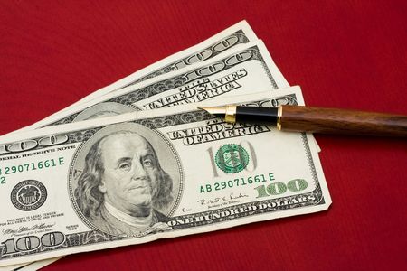 A pen sitting on one hundred dollar bills on a red background, Having a written budgetの写真素材