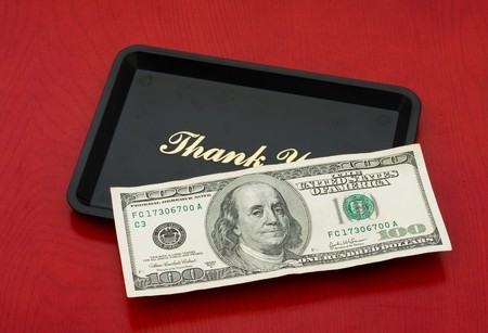 A one hundred dollar bill on a black tray on a wood background, tip moneyの写真素材