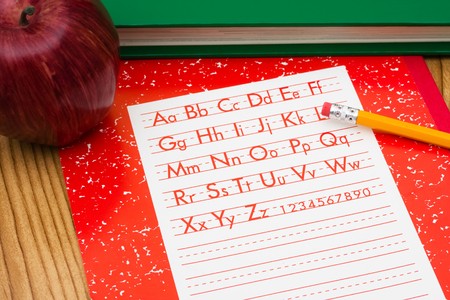 A pencil on a workbook with an apple and a book, school work