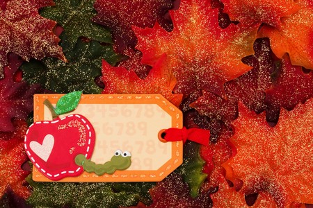 Fall leaves with a blank tag with apple and worm on it on a brown background, Back to school