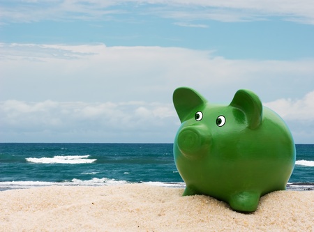 A green piggy bank in the sand at the beach, Vacation Savingsの写真素材