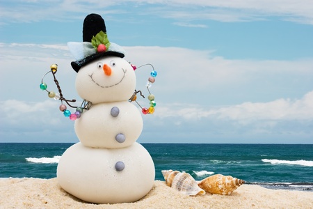 A snowman with seashells sitting on the sand with water, winter vacationの写真素材