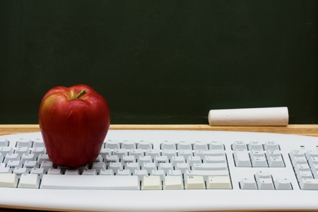 Computer keyboard on a desk with an apple in front of a chalkboard with copy space, E-learningの写真素材