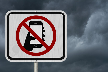 No Texting and Driving Sign, White Information sign with symbol of a hand and texting with stormy sky backgroundの写真素材