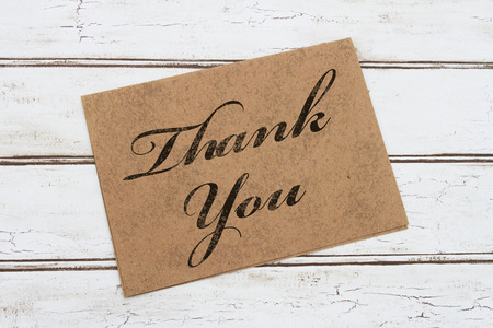 A thank you card, A brown card with words Thank You over a distressed wood backgroundの写真素材