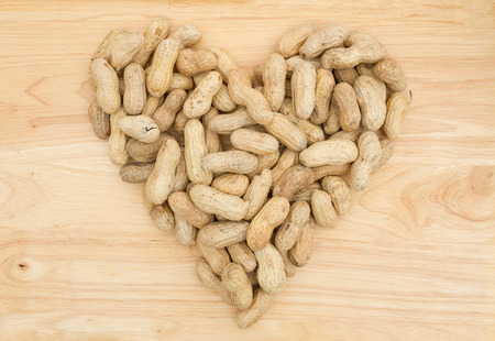 Peanuts are a healthy snack, Raw peanuts in shells in the shape of a heart on wood