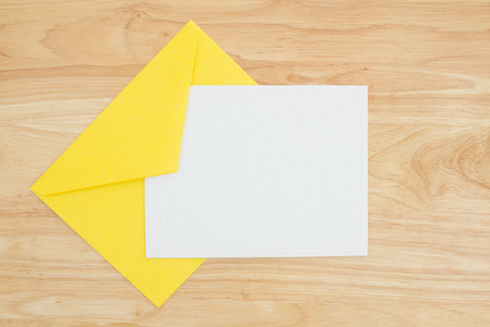 An embossed blank white card with yellow envelope on a desk with copy space for your messageの写真素材