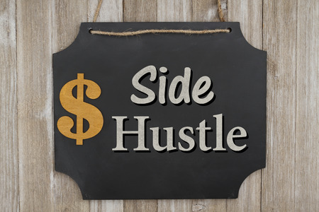 Making money with your side hustle, Hanging chalkboard with a dollar sign on weathered wood wall with text Side Hustleの写真素材
