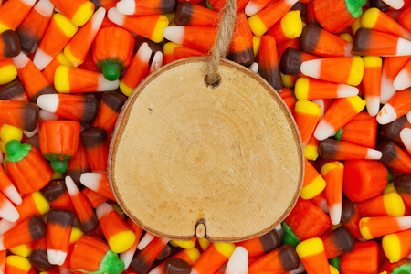 Halloween candy corn with candy pumpkins background with wood plaque for your message