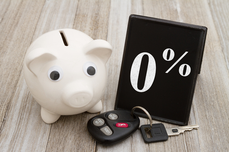 A piggy bank with retro freestanding chalkboard  with car key on weathered wood with text 0%