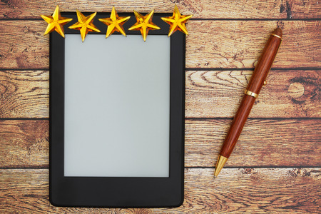 A blank e-reader on a old desk with a pen and five gold stars that you can use as a mock up for your messageの写真素材