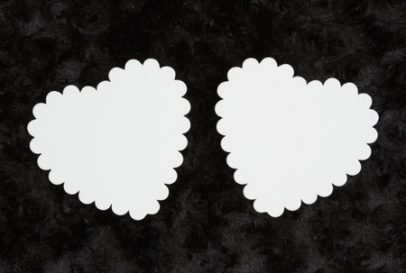 Two blank white hearts on black rose textured plush fabric you can use the hearts for your messageの写真素材