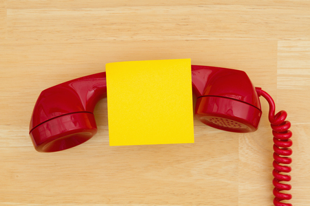 Retro red phone handset with sticky note on textured wood desk with copy space for your messageの写真素材