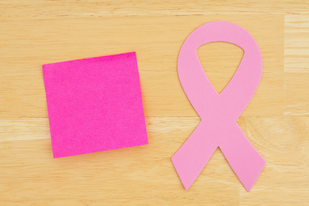 Pink cancer ribbon with sticky note on textured desk wood  with copy space for your cancer messageの写真素材