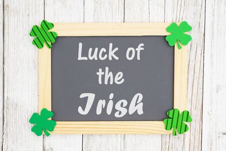 Luck of the Irish text on a chalkboard with green shamrocks on weathered whitewash textured woodの写真素材