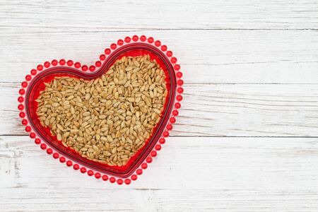 Sunflower seeds in a red bowl for the health benefits of the snack  on weathered whitewash wood