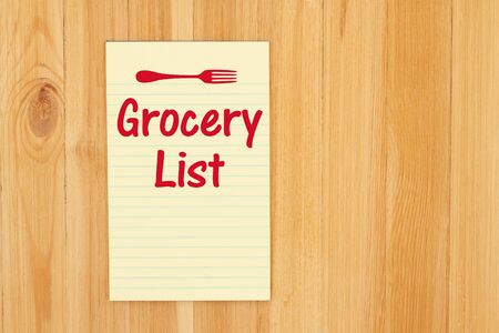 Grocery list message with a fork on a yellow legal notepad paper on wood deskの写真素材