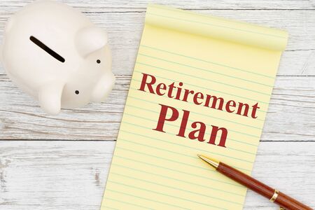 Writing down your retirement plan with a piggy bank, notepad and pen on weathered whitewash wood with grain textureの写真素材