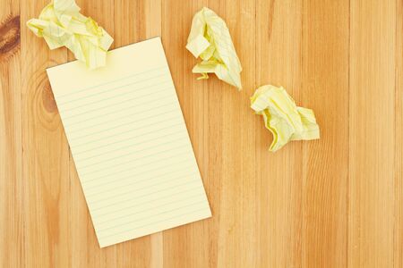 Yellow legal notepad paper with crumpled paper on pine wood desk with copy space for your business or writing message or mockupの写真素材