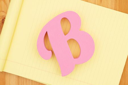 Capital pink letter B on yellow lined paper on a wood deskの写真素材