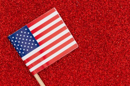 Closeup of a small American paper flag on red glitter textured paper with a very shallow depth of fieldの写真素材