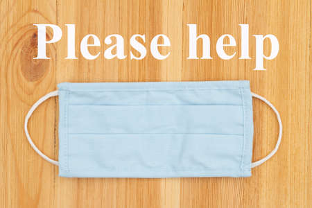Please help word message on blue cloth face mask on a wood desk for your covid-19 message