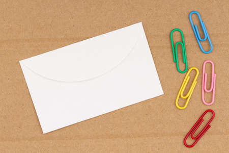 Blank envelope on brown textured cardboard with paperclips background with copy space for messageの写真素材